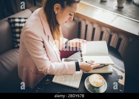 Arbeiten Sie bequem in einem Café. Freiberufliche Frau blättert durch die Seiten eines Tagebuchs in einem Café. Attraktive Frau, die im Restaurant Kaffee trinkt Stockfoto