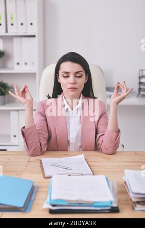 Junge ernsthafte weibliche Büroleiterin Yoga am Schreibtisch üben, während Pause nach der Arbeit mit Finanzdokumenten oder die Analyse von Daten Stockfoto