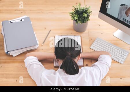 Rückansicht der jungen, müden Geschäftsfrau, die auf dem Schreibtisch mit ihrem Gesicht auf Dokumenten liegt, während sie nach einem harten Arbeitstag im Büro beim Nickerchen anschlagt Stockfoto