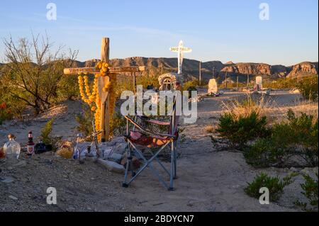 Ein Campingstuhl sitzt an einem Grab auf dem Terlingua Cemetery in West Texas, wo die Gräber von handgefertigten Verzierungen markiert sind. Stockfoto