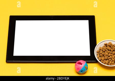 Kaufen Sie Tiernahrung und Spielzeug online über die App auf Ihrem Tablet, auf einem gelben Hintergrund mit einer Kopie des Raumes. Das Konzept des Online-Shopping, elektronische p Stockfoto