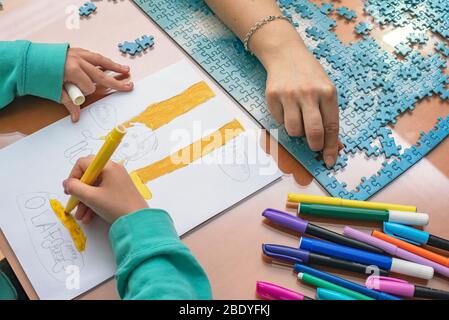 Einige Hände machen ein Puzzle, während andere ein Bild zeichnen Stockfoto