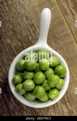 Frisch gepflückte Erbsen in einer weißen Schüssel auf einem Holztisch. Stockfoto