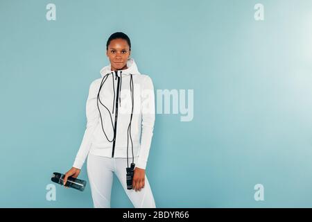 Weibliches Fitness-Modell mit Springseil und Wasserflasche auf blauem Hintergrund Stockfoto