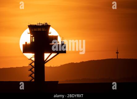 10. April 2020, Hessen, Frankfurt am Main: Die Sonne geht hinter dem Turm der Deutschen Flugsicherung (DFS) am Frankfurter Flughafen unter, ohne dass Flugzeuge am Himmel stehen. Der reguläre Flugbetrieb ist aufgrund der weltweiten Corona-Pandemie fast zum Stillstand gekommen. Foto: Boris Roessler/dpa Stockfoto