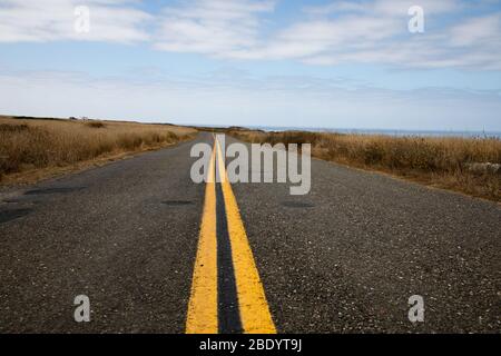 Blick auf eine zweispurige Straße in Richtung Pazifik mit Grasland auf beiden Seiten und Wolken über dem Ozean Stockfoto