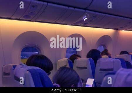 Flugzeugkabine mit Passagieren in Stühlen während eines Abendfluges. Reihe von Ebenen Sitzen am Fenster. Weicher Fokus und verschwommenes Foto Stockfoto