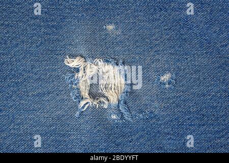 Nahaufnahme des ausgefransten Lochs in blauer Denim-Qualität Stockfoto