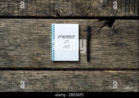 Notizblock mit einer Erinnerung an die Live-Nachricht in ihm auf rustikalem Holzhintergrund mit schwarzem Marker daneben platziert. Stockfoto