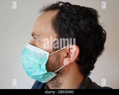 Seitenansicht einer Person (Mann / Mann), die eine grüne Operationsmaske oder Gesichtsmaske (Mund / Nase) zum Infektionsschutz trägt, z.B. Corona-Virus Covid-19 Stockfoto