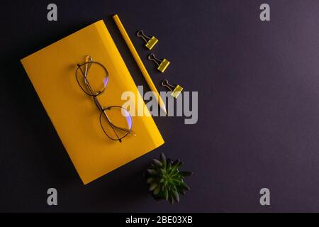 Gelber Bleistift, gelbes Notizbuch und Brille, Stifte, Clip-Papier auf schwarzem Hintergrund Stockfoto