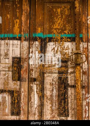 Nahaufnahme einer alten hölzernen, abblätternden, bemalten Türplatte und verrosteten Metallstange in warmen Farben Stockfoto