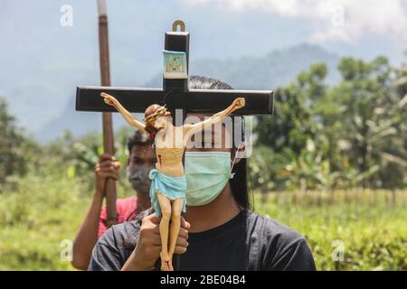 Sleman, Yogyakarta, Indonesien. April 2020. Eine junge Katholikin trägt eine Maske und hält das Kreuz Jesu im Hintergrund des Merapi-Berges, während sie den stillen Kreuzweg von Karfreitag vier jungen Katholiken in Sleman führt. Ostern und andere Gottesdienste für Christen und Katholiken auf der ganzen Welt 2020 unterbrochen durch den Ausbruch des Corona oder Covid-19 Virus. Kredit: Slamet Riyadi/ZUMA Wire/Alamy Live News Stockfoto