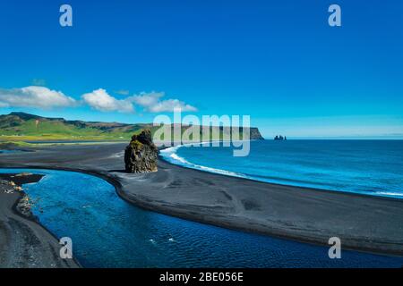 Berühmte Dyrholaey Felsformationen und schwarzer Sandstrand in der Nähe von Vik Island an sonnigen Tagen. Klar blauer Himmel mit Lavastein Reynisdrangar im Hintergrund. Blau Stockfoto