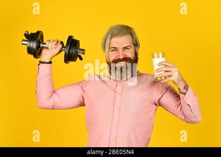 Quelle von Kalzium. Bärtiger Mann trinkt Milch. Trainieren Sie im Fitnessstudio. Milch gute Nährstoffe. Menge an Fett. Vitamine für Muskeln. Sportler halten Hantel und Glas Milch. Protein-Diät. Protein-Cocktail. Stockfoto