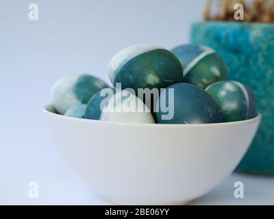 Ostereier mit einem roten Kohl natürliche Farbe auf einem weißen Hintergrund mit leeren Raum mit weißen Frühlingsblumen in einer hellblauen Schüssel verziert gefärbt. Stockfoto