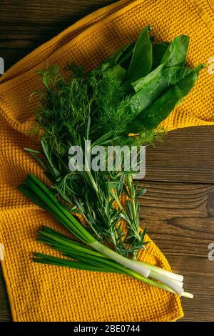 Gemischtes Grün, frische, Gartenkräuter. Spinat, Rosmarin, Dill und grüne Zwiebeln auf einem orangefarbenen Handtuchständer auf einem Holztisch. Draufsicht, Nahaufnahme Stockfoto