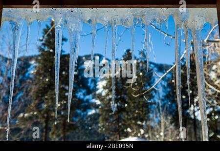 Eiszapfen hängen vom Dach und sehen von innen ein Fenster mit Blick nach draußen. Stockfoto