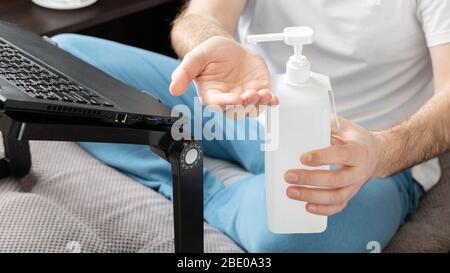 Junger kaukasischer Mann in Schutzmaske, der die Hände mit Desinfektionsmittel reinigt. Coronavirus Covid 19 Schutz Handhygiene. Freiberufler Remote-Arbeit zu Hause Stockfoto