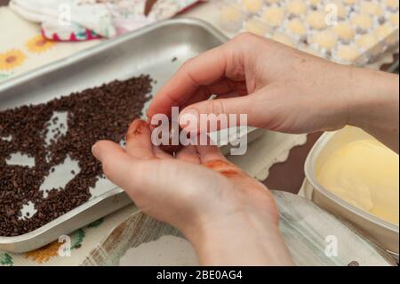 Nahaufnahme von Frauenhänden, die köstliche und traditionelle „Brigadeiros“ (brasilianische Fudge Balls) auf einem Aluminiumtablett machen. Draufsicht. Horizontale Aufnahme. Stockfoto