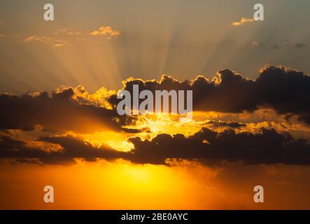 Zwei Schichten Wolken mit Sonne, die hinter dem Licht scheint und wunderschöne Sonnenstrahlen von hinten hinterlässt. Dramatischer Sonnenuntergang Himmel mit lebendigen Farben. Stockfoto