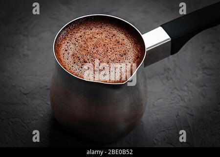 Kaffee mit braunem Schaum, gebraut in Zezve auf dunkelgrauem Hintergrund Stockfoto