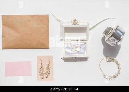 Hochzeit Accessoires Hintergrund. Goldene Eheringe und feminine Accessoires. Goldenes Lametta, Schachtel, Ohrringe, Umschlag, Ringe, Halskette, Armband auf wh Stockfoto