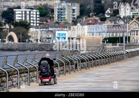 Ein Mann auf einem Mobilitäts-Roller fährt während der Sperrung des Coronavirus im Vereinigten Königreich entlang der Royal Parade am Grand Pier in Weston-super-Mare vorbei. Stockfoto