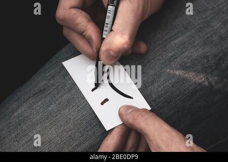 Schreiben sehr traurig Lächeln Emoji auf weißem Papier Karte in Händen auf Jeans Textur Farbe abgestuften Hintergrund. Traurige Stimmung schlecht farblose Zeit Stockfoto