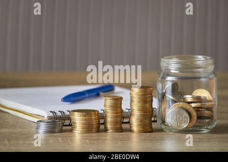 Reihen von Münzen und Jar-Münzen auf Holztisch mit grauem Hintergrund, Geldsparkonzept Stockfoto