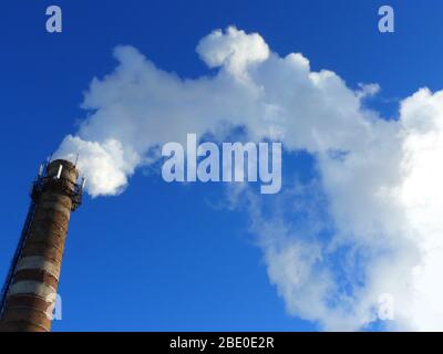 Rohre einer alten Fabrik werfen Wolken von giftigem weißem Rauch in den Himmel, die die Atmosphäre schädigen. Urbaner Smog aus Rauch aus Kesselhäusern. Weißer Rauch aus einem Kamin gegen einen blauen klaren Himmel. Stockfoto