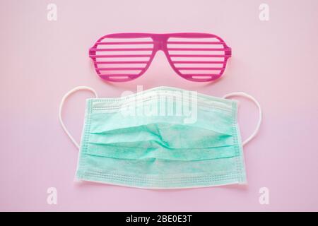 Optimistische Coronavirus-Szene. Rosa Sonnenbrille und medizinische Maske auf rosa Pastellhintergrund. Warten Frühling/Sommer Zeit. Mode, Design, Urlaubslandschaft. Stockfoto