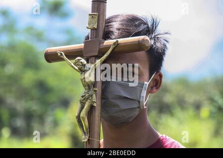 Sleman, Yogyakarta, Indonesien. April 2020. Ein katholischer junger Mann trägt eine Maske und hält das Kreuz Jesu vor dem Hintergrund des Merapi-Berges, während er den Weg zum stillen Kreuz von Karfreitag vier jungen Katholiken führt. Ostern und andere Gottesdienste für Christen und Katholiken auf der ganzen Welt 2020 unterbrochen durch den Ausbruch des Corona oder Covid-19 Virus. Kredit: Slamet Riyadi/ZUMA Wire/Alamy Live News Stockfoto