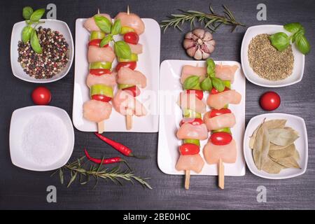 Rohes Hähnchenspieß mit Tomaten und Gemüse. Draufsicht. Hähnchenkebabs mit Tomaten und Gewürzen auf einem weißen Teller. Stockfoto