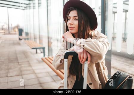 Nachdenkliche stilvolle Mädchen in einem Mantel und Hut sitzt an einer Haltestelle warten Bus Stockfoto