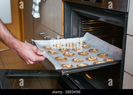 Junger Mann, der die hausgemachten Kekse in den Ofen stellt Stockfoto