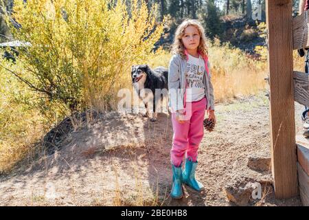Mädchen mit Kiefernzapfen im Herbst mit Hund im Feld stehend Stockfoto