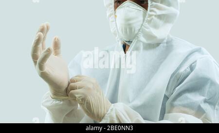 Arzt mit Maske und weißem Bioprotective Anzug, der Latexhandschuhe auf die Hände auf weißem Hintergrund legt Stockfoto