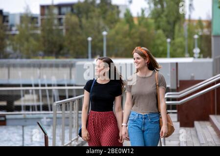 Zwei junge Frauen, die an einem Yachthafen entlang laufen und nach links schauen Stockfoto