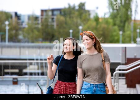 Zwei junge Frauen, die an einem Yachthafen entlang laufen und nach links schauen Stockfoto