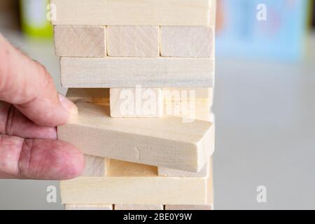 Ein Mann entfernt vorsichtig einen Holzblock aus einem Jenga-Turm Stockfoto