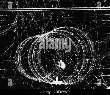 Kreisförmige Spur von 42 Meu Positron in 12,000 Gauß Magnetfeld. Die Weglänge der Positronenbahn auf diesem Foto beträgt fast 8 Meter. Elektronen- und Positronenspiralbahnen in einer Wolkenkammer im Lawrence Berkeley Laboratory, Kalifornien. Elektron und Positron begannen ihr Leben am unteren Rand des Rahmens; sie wurden durch einen von rechts eintretenden Gammastrahl erzeugt. Das Positron, ein Elektron mit positiver Ladung, spiraliert (größere Schleifen) in die linke untere Ecke, während sich die kleineren Schleifen des Elektrons nach oben bewegen. Die anderen Spuren, die den Rahmen überqueren, sind ebenfalls darauf zurückzuführen Stockfoto