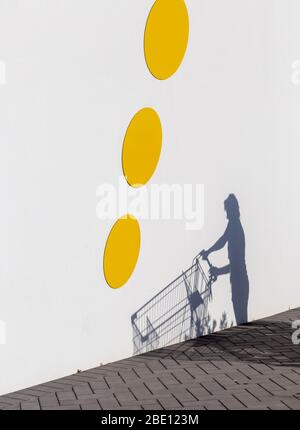 Schatten auf einer weißen Wand eines leeren Einkaufswagens, der geschoben wird. Drei große gelbe Kreise an der Wand Stockfoto