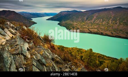 Halbmondförmiger, milchig-grüner Kanas-See, umgeben von Altay-Bergketten mit Herbstlaub. Stockfoto