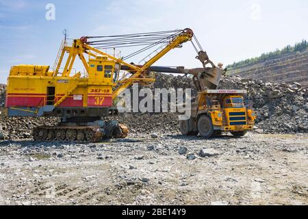 Ein Bergwerksbagger lädt einen riesigen LKW mit Granitgestein Stockfoto