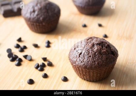 Schokoladenmuffins, Schokoladenchips, Schokoriegel, Tasse Kaffee, Teekanne auf einer Holzfläche mit warmem Schal, Weihnachtsbeleuchtung Bokeh und Stolly in der Stockfoto