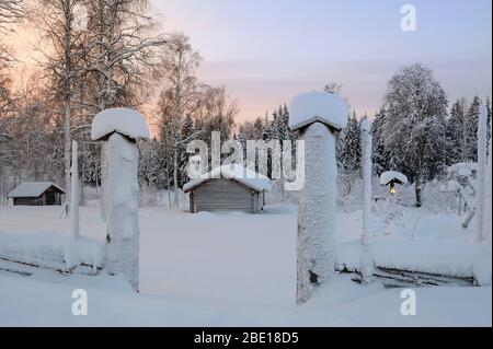 Pfosten und Blockhäuser in einer sonnenbeschwingen Winterlandschaft Stockfoto