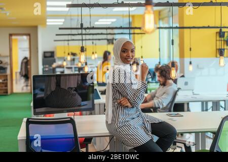 Trait einer schwarzen (afroamerikanischen) weiblichen muslimin, die in einem modernen Geschäftsbüro steht, während sie einen Hijab trägt. Stockfoto