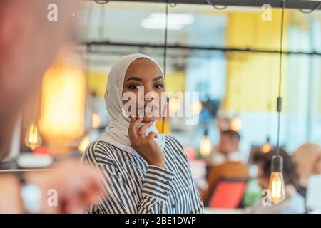 Trait einer schwarzen (afroamerikanischen) weiblichen muslimin, die in einem modernen Geschäftsbüro steht, während sie einen Hijab trägt. Stockfoto