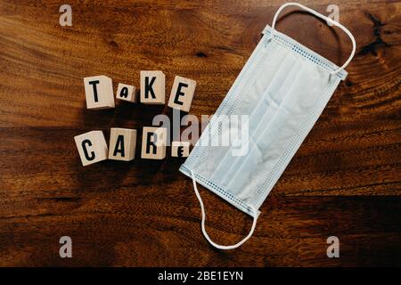 'Take care' Text aus Holz mit medizinischem Maskenwürfel auf Holzhintergrund. Stockfoto